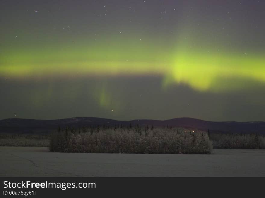 Some color of aurora borealis in the sky over distant frozen forest in Alaska. Some color of aurora borealis in the sky over distant frozen forest in Alaska