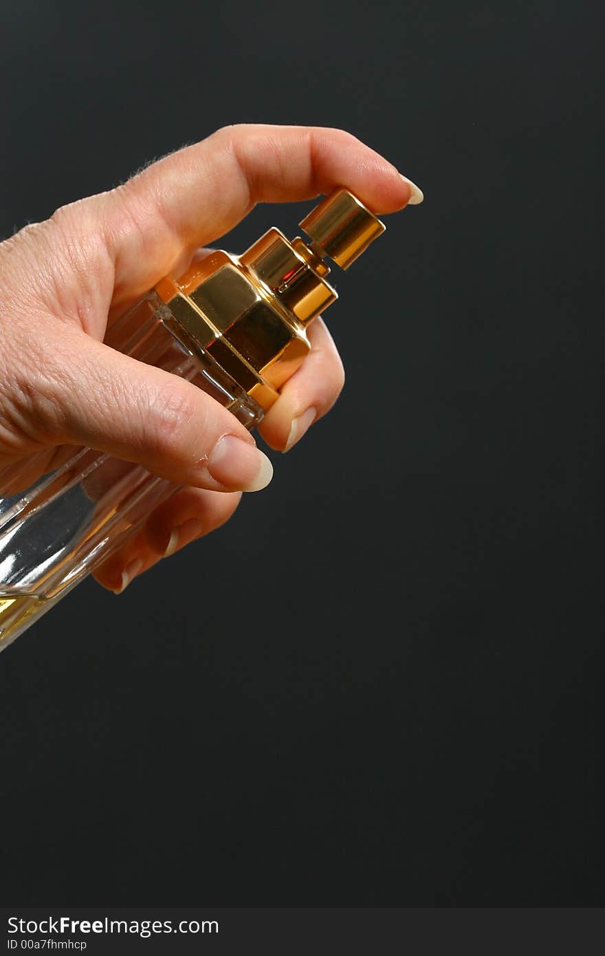 Older female hand spraying perfume against a dark background