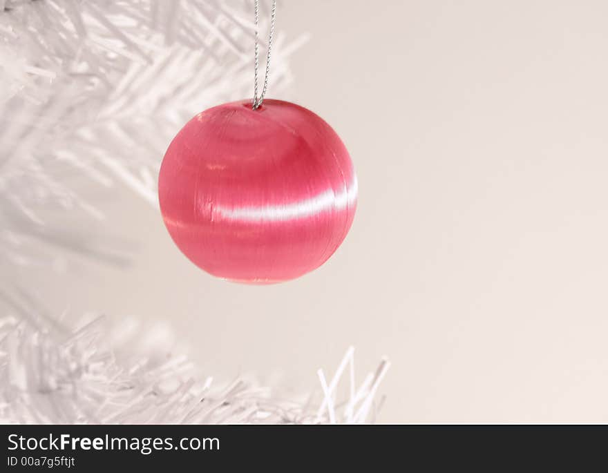 Icy pink Christmas ornament hanging from branch of modern white artificial tree. Icy pink Christmas ornament hanging from branch of modern white artificial tree