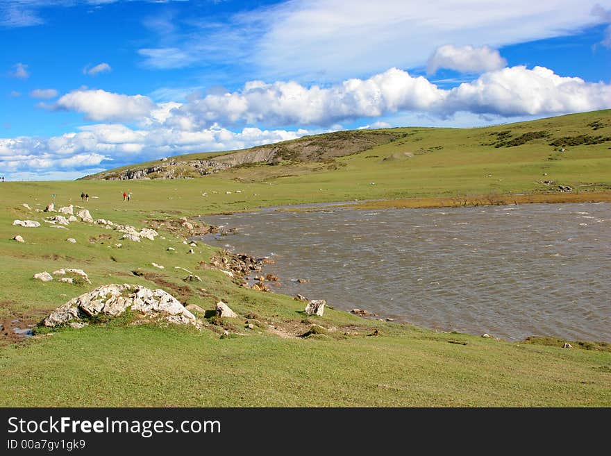 Green hill with a lake beneath a cloudy blue sky. Green hill with a lake beneath a cloudy blue sky