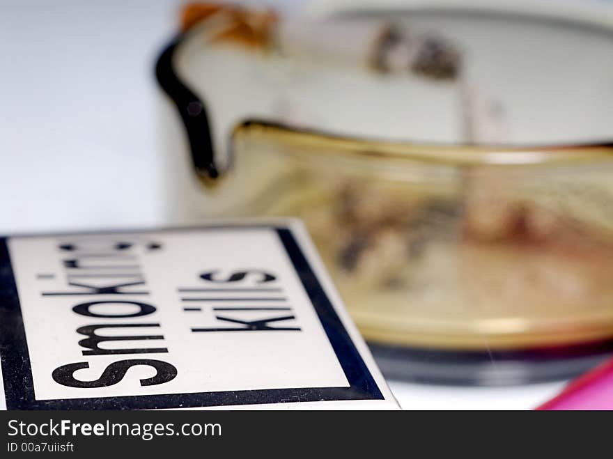 Picture of half burned cigarette in ash tray with pack of cigarettes with visible sign Smoking kills and lighter.