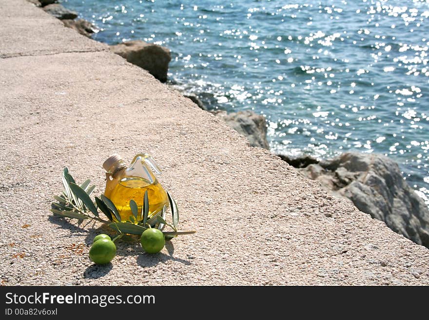 Small bottle of olive-oil an an olive-branch with fruits on it in front of a mediterranean scene. Small bottle of olive-oil an an olive-branch with fruits on it in front of a mediterranean scene