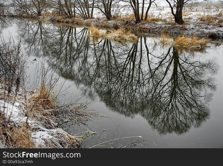 The country river in the beginning of winter with reflection of a local landscape