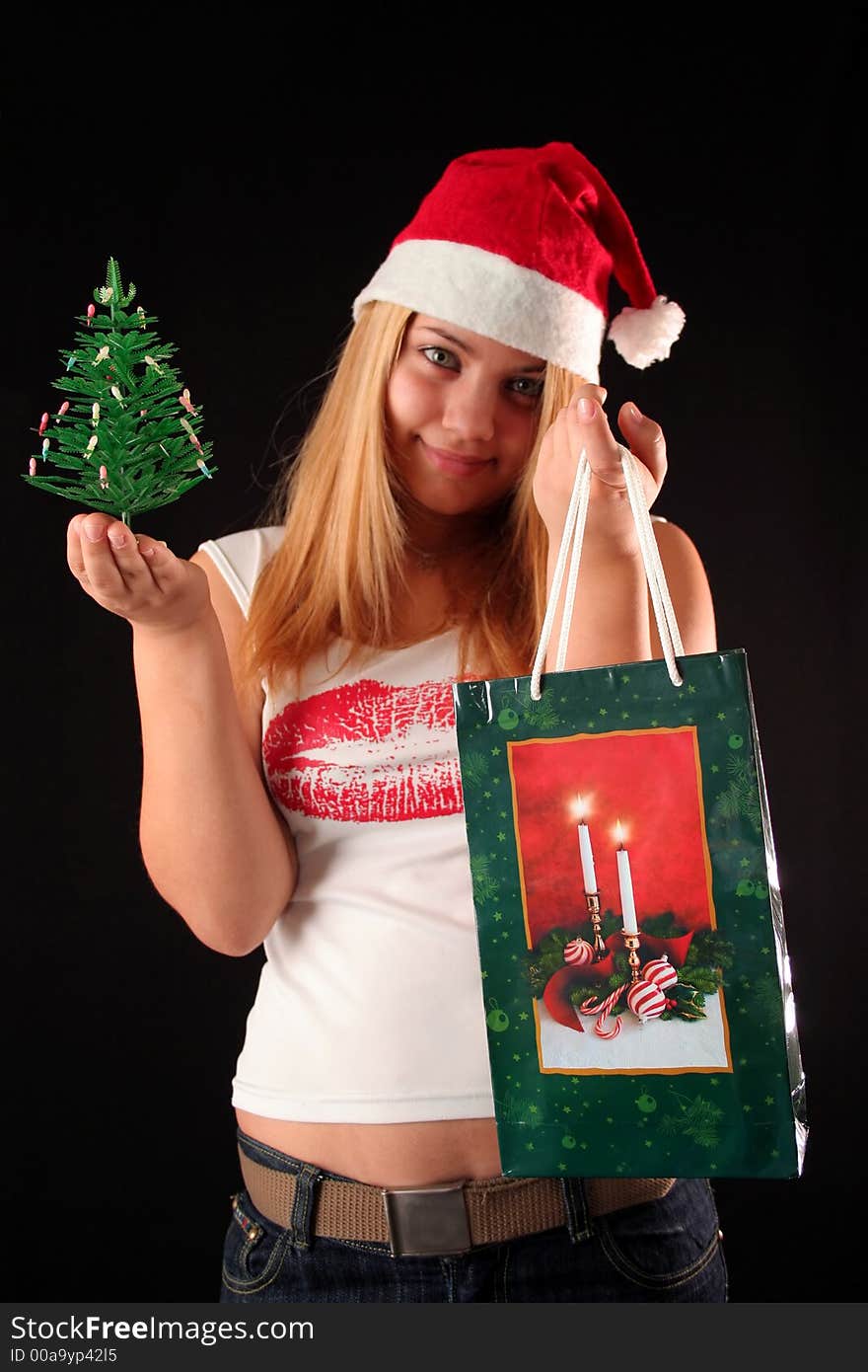 Christmas blonde girl offer a little Christmas-tree and a gift in a bag, black background. Christmas blonde girl offer a little Christmas-tree and a gift in a bag, black background