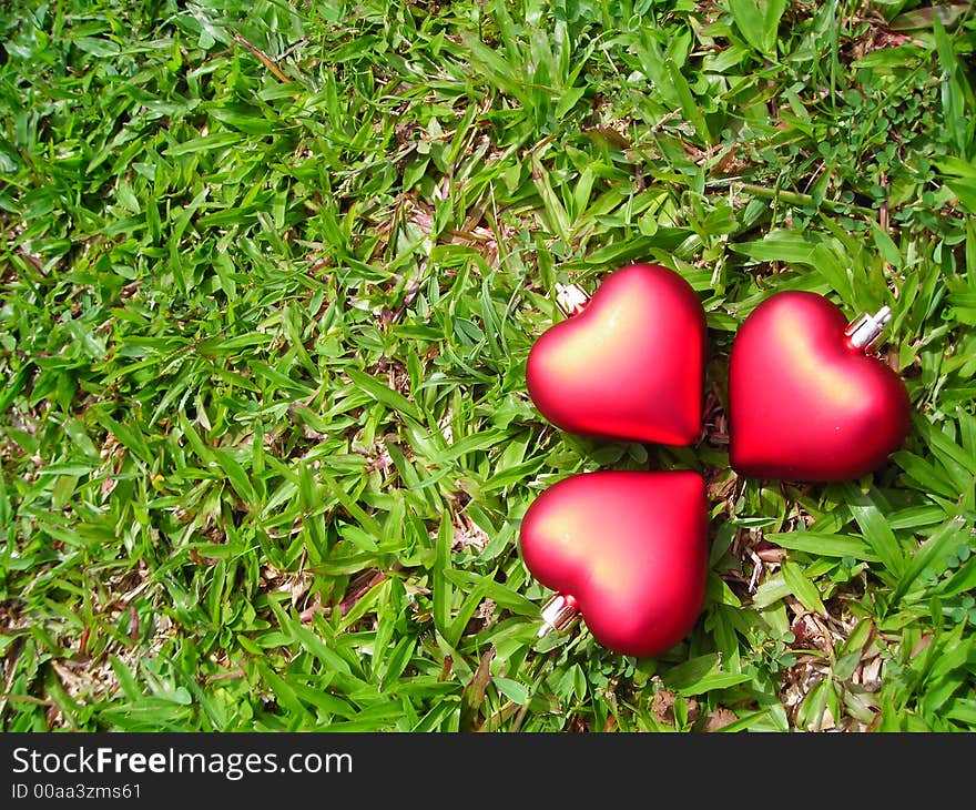 Three hearts made of christmas decoration symbolising friendship on green grass background with copyspace. Three hearts made of christmas decoration symbolising friendship on green grass background with copyspace