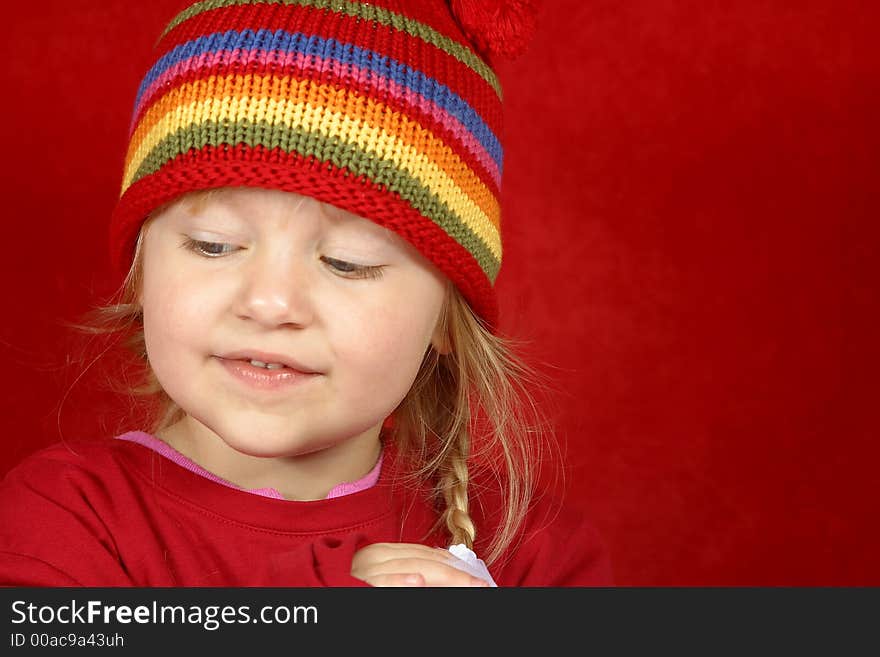 A cute little girl with a red and multi color-striped hat on a red background