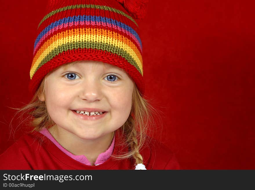 A cute little girl with a red and multi color-striped hat on a red background