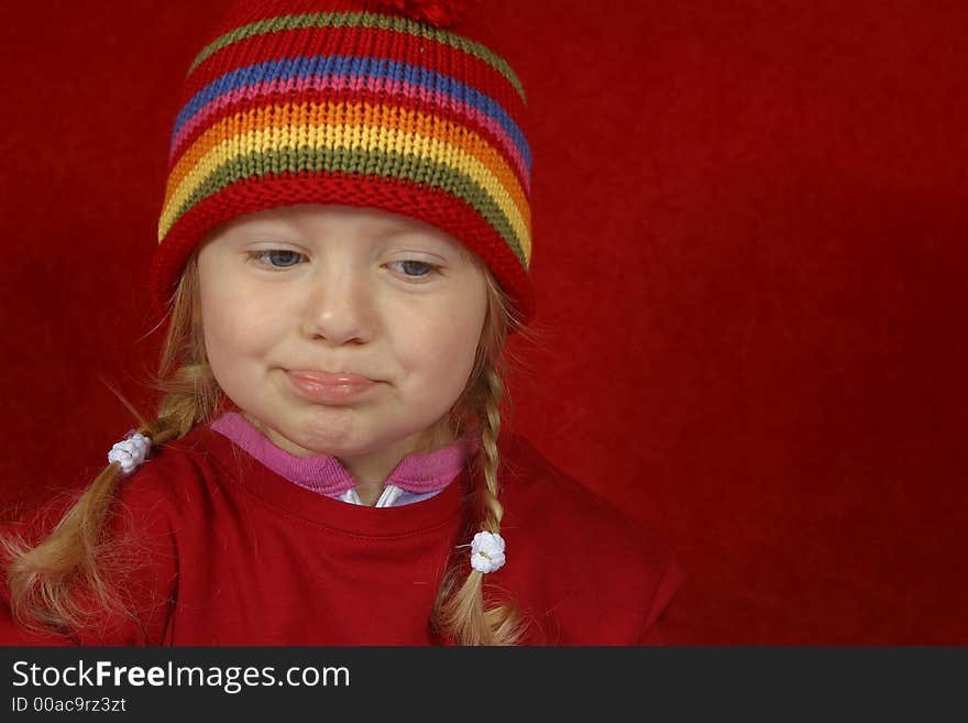 A cute little girl with a red and multi color-striped hat making silly faces