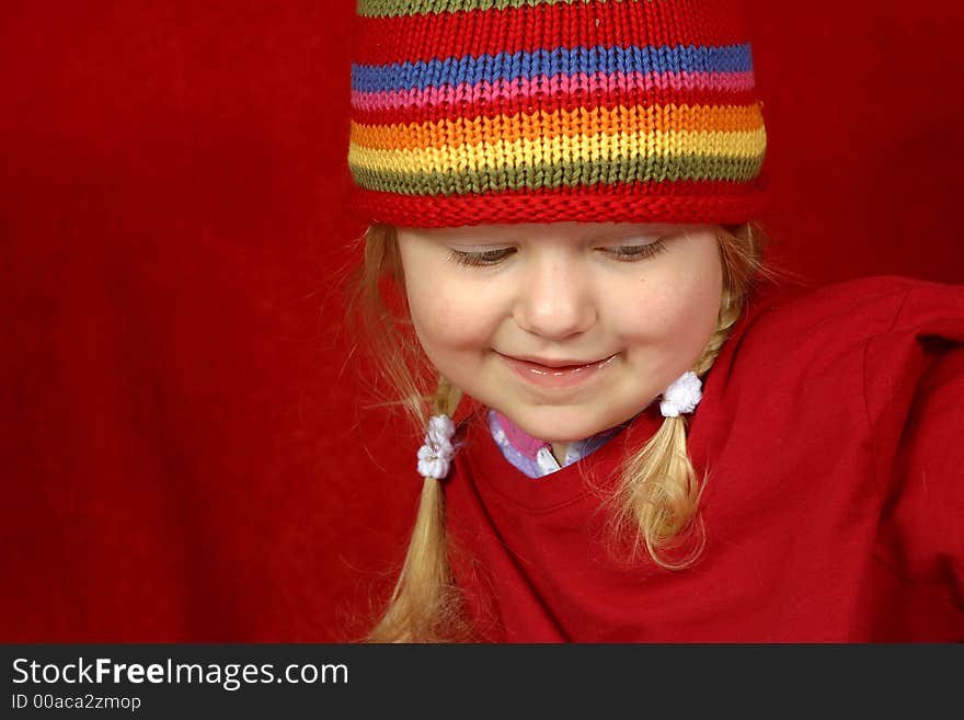 A cute little girl with a red and multi color-striped hat on a red background