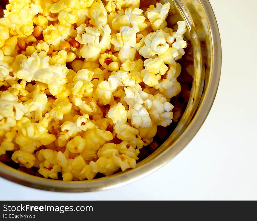 Buttered popcorn in a metal bowl on a white background