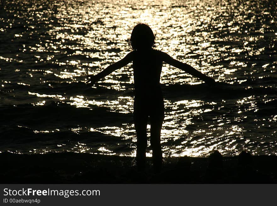 Young girl standing in surf at sunset. Young girl standing in surf at sunset