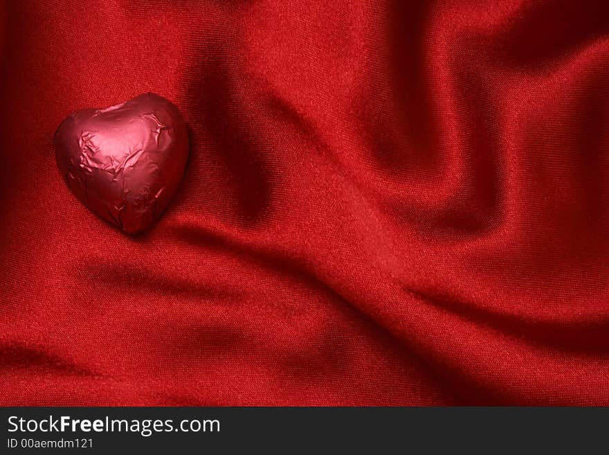 Red heart shaped foiled chocolate on red satin. Red heart shaped foiled chocolate on red satin