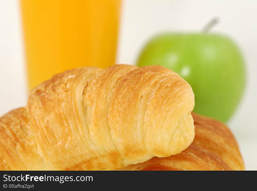 Fresh-baked croissant, orange juice and green apple.  Shallow DOF. Focus on croissant. Fresh-baked croissant, orange juice and green apple.  Shallow DOF. Focus on croissant.