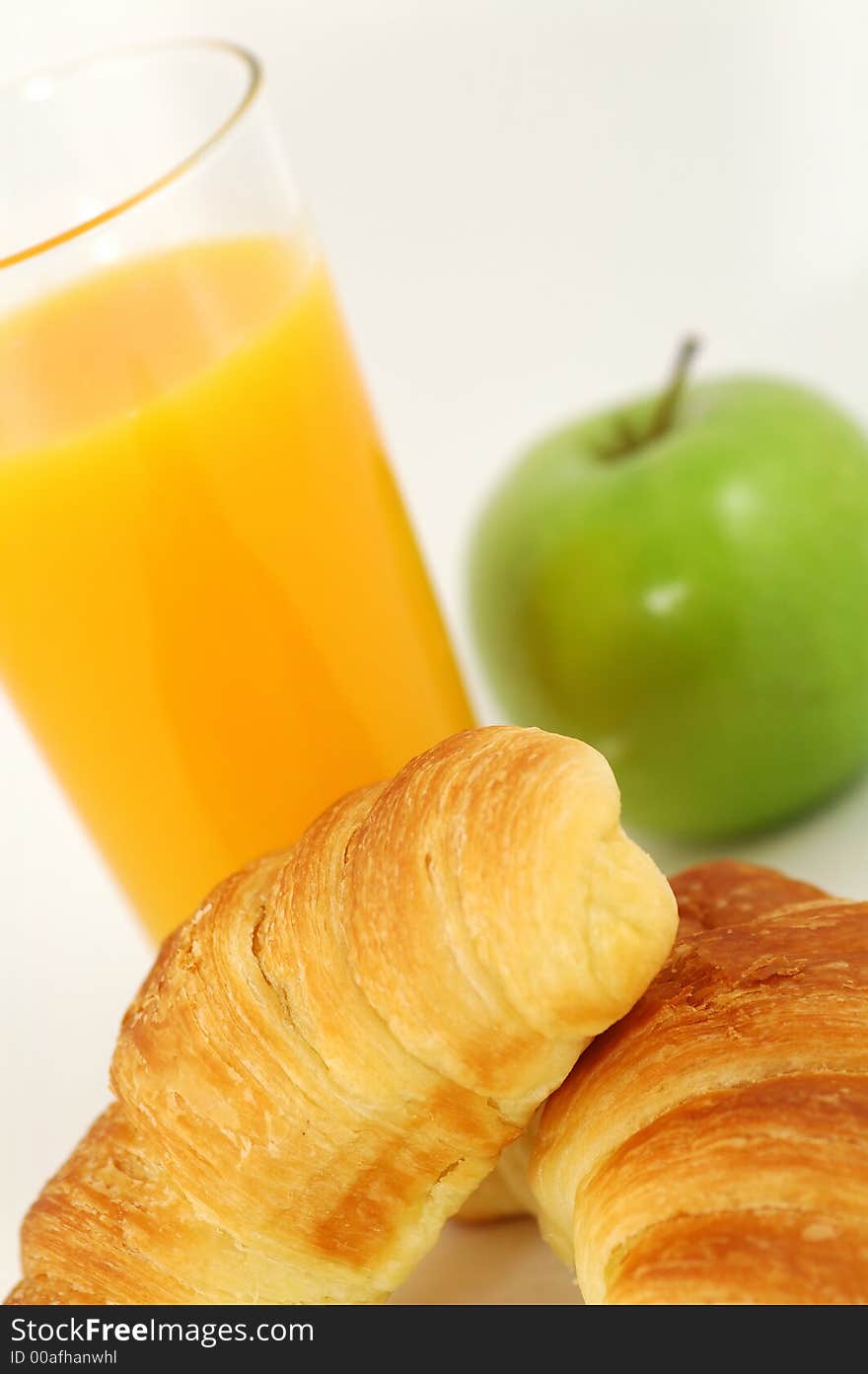 Fresh-baked croissant, orange juice and green apple.  Shallow DOF. Focus on croissant. Fresh-baked croissant, orange juice and green apple.  Shallow DOF. Focus on croissant.