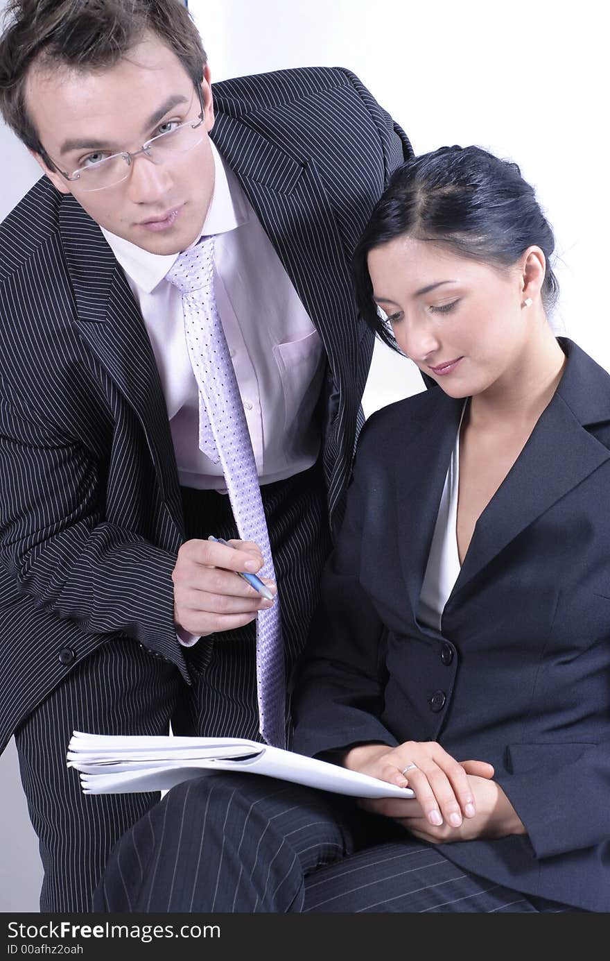 Picture of standing standing man business reading notes and woman sitting on chair and holding notes and pen, both business dressed. Picture of standing standing man business reading notes and woman sitting on chair and holding notes and pen, both business dressed.