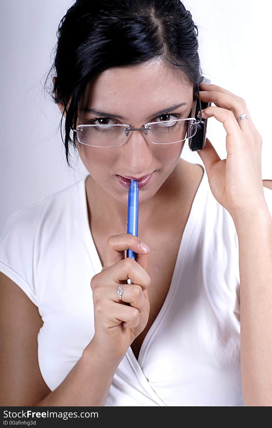 Picture of woman with glasses holding a mobile phone in one hand and pen in other and listening. Picture of woman with glasses holding a mobile phone in one hand and pen in other and listening.