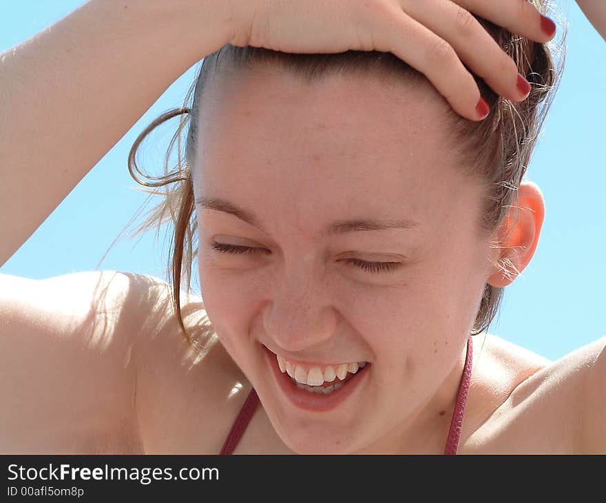 A closeup of a young woman pulling her hair away from her face while laughing. A closeup of a young woman pulling her hair away from her face while laughing