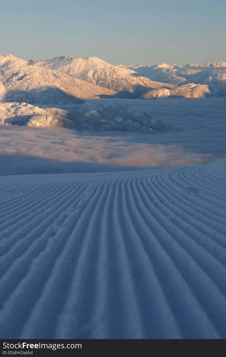 A groomed ski run seemingly disappears into a valley of cloud. A groomed ski run seemingly disappears into a valley of cloud.