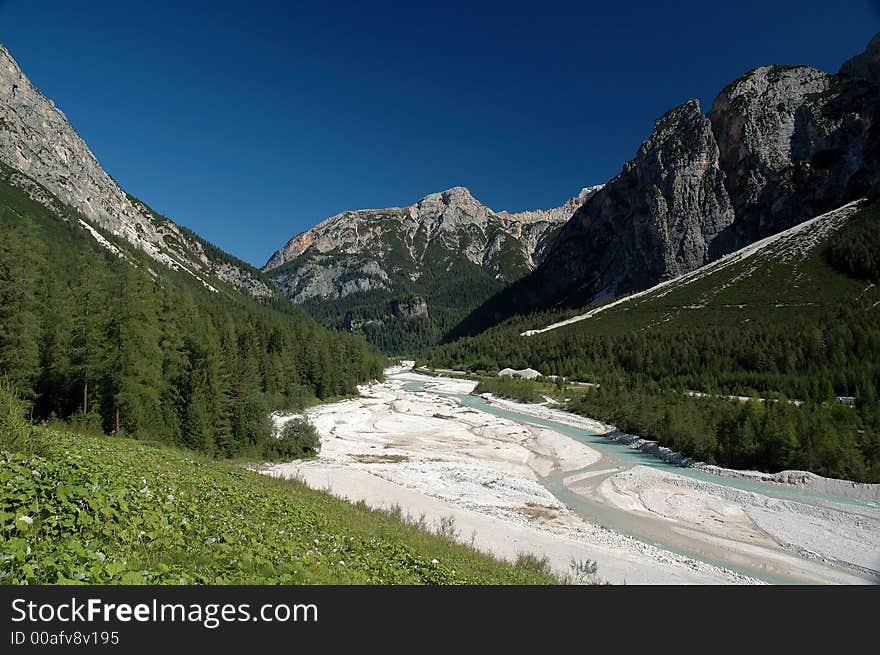 Mountain river with wide riverbed with Dolomiti mountains in Italy in background.