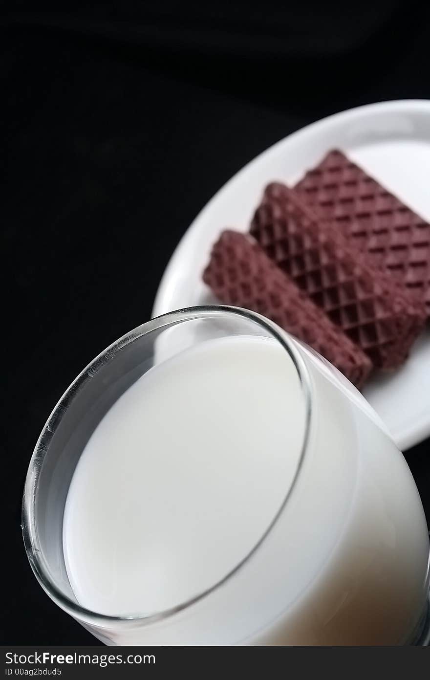 Chocolate cookies and milk over black background