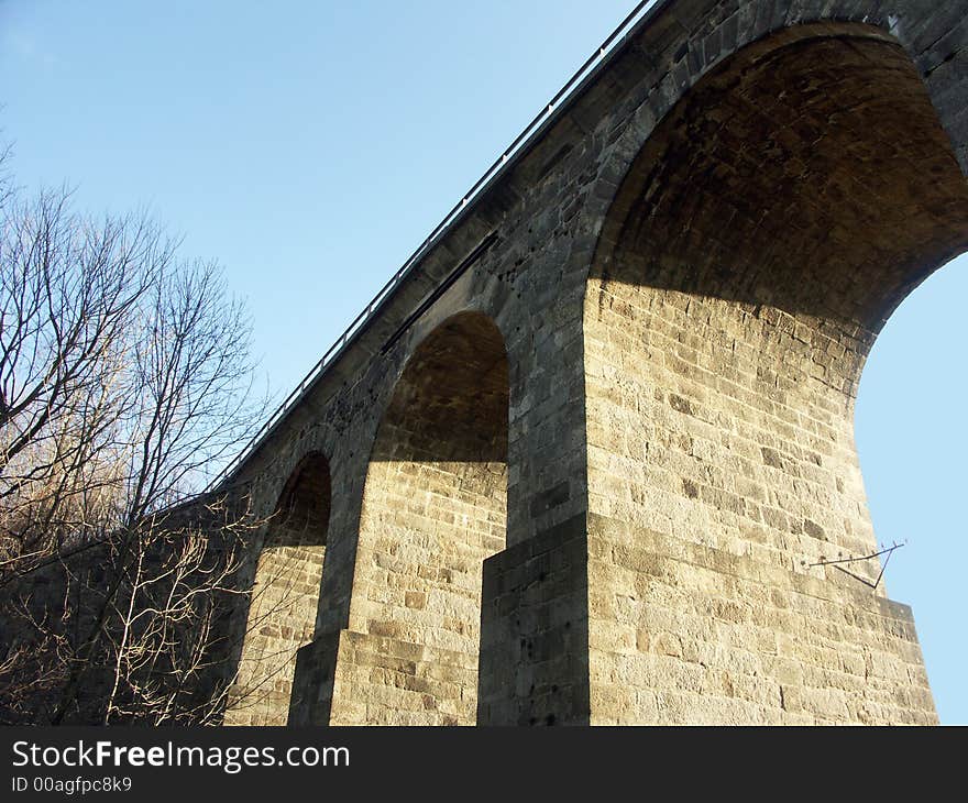 Very old stone bridge with three arch supports and a road passing through one arch. Very old stone bridge with three arch supports and a road passing through one arch.