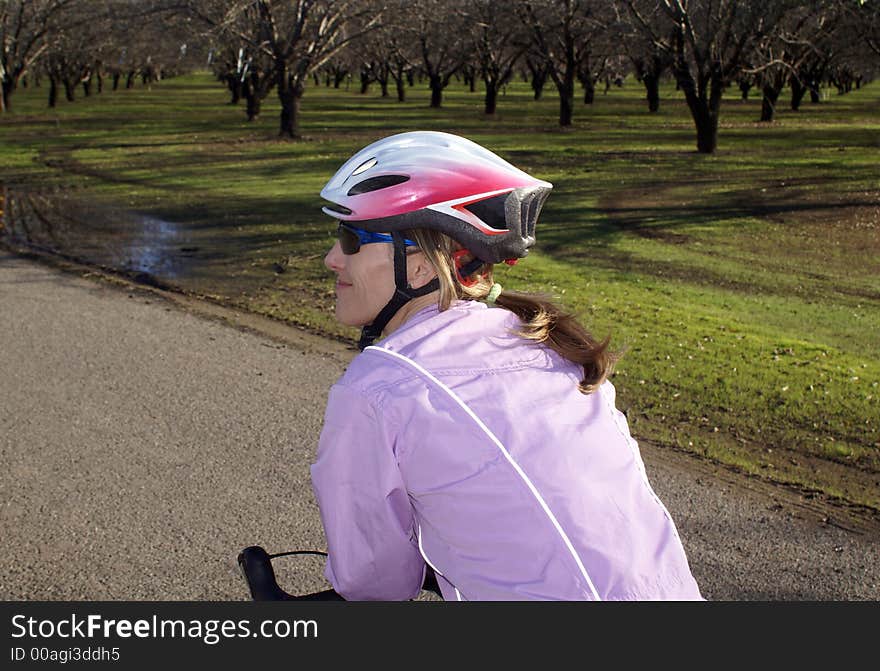 Woman on bike smiling and leaning on handlebars in lavendar jacket stopped by an almond orchard. Woman on bike smiling and leaning on handlebars in lavendar jacket stopped by an almond orchard.