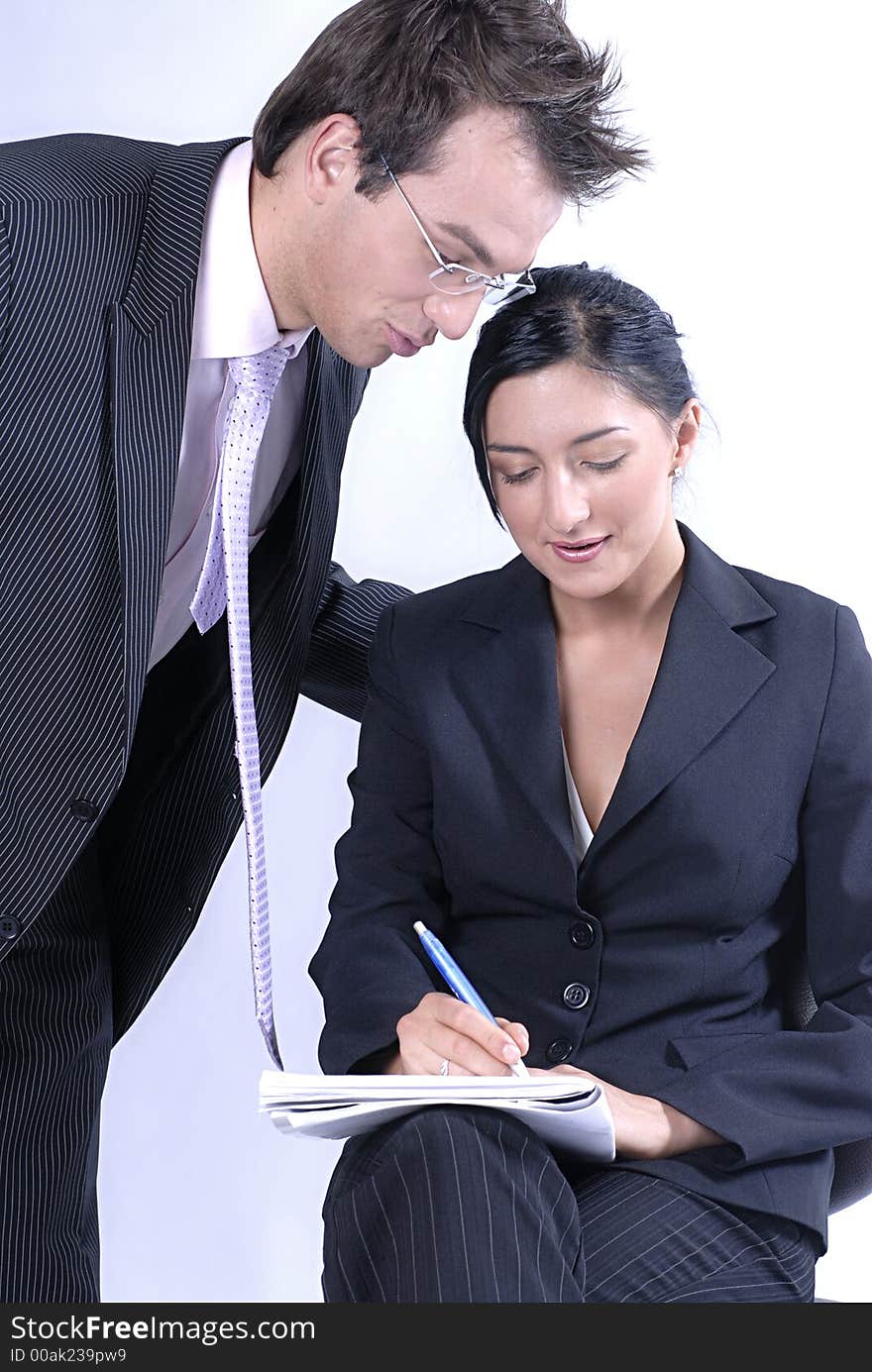 Picture of standing standing man business reading notes and woman sitting on chair and holding notes and pen, both business dressed. Picture of standing standing man business reading notes and woman sitting on chair and holding notes and pen, both business dressed.