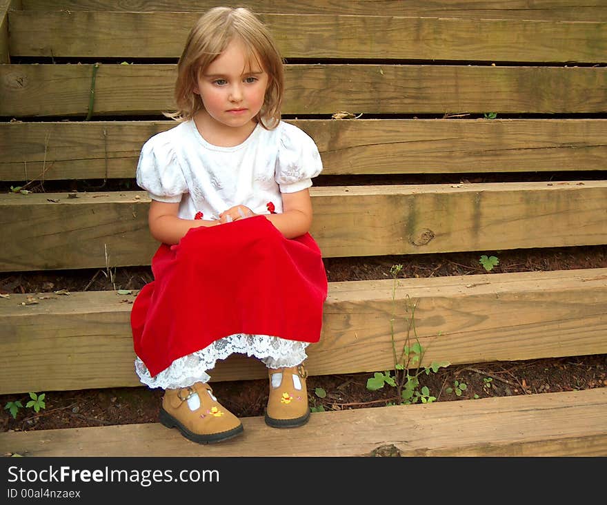 Little girl in red dress sitting on steps thinking