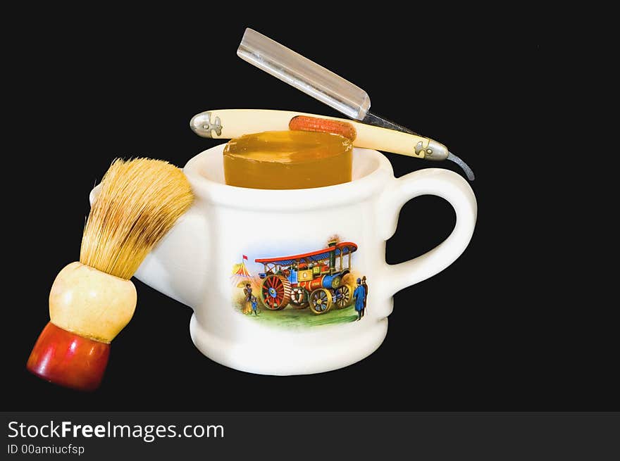 A white antique shaving mug with a handle on one end, a brush holder on the other, a 1890s scene on the side, a brush and a straight razor, all on a black background. A white antique shaving mug with a handle on one end, a brush holder on the other, a 1890s scene on the side, a brush and a straight razor, all on a black background.