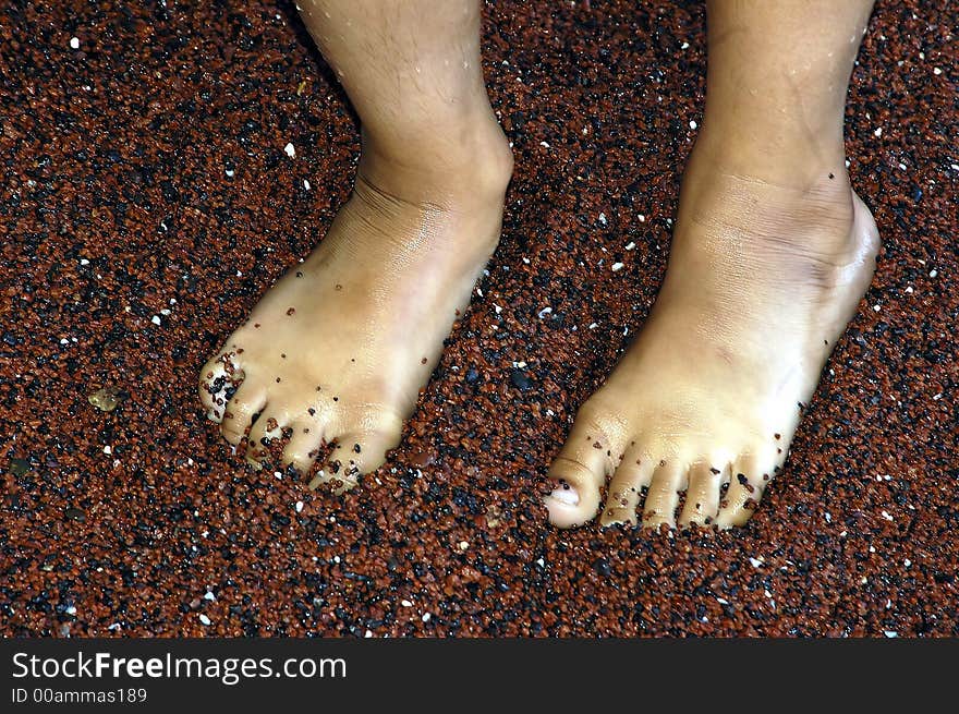 Wet feet of a kid on a red sand beach