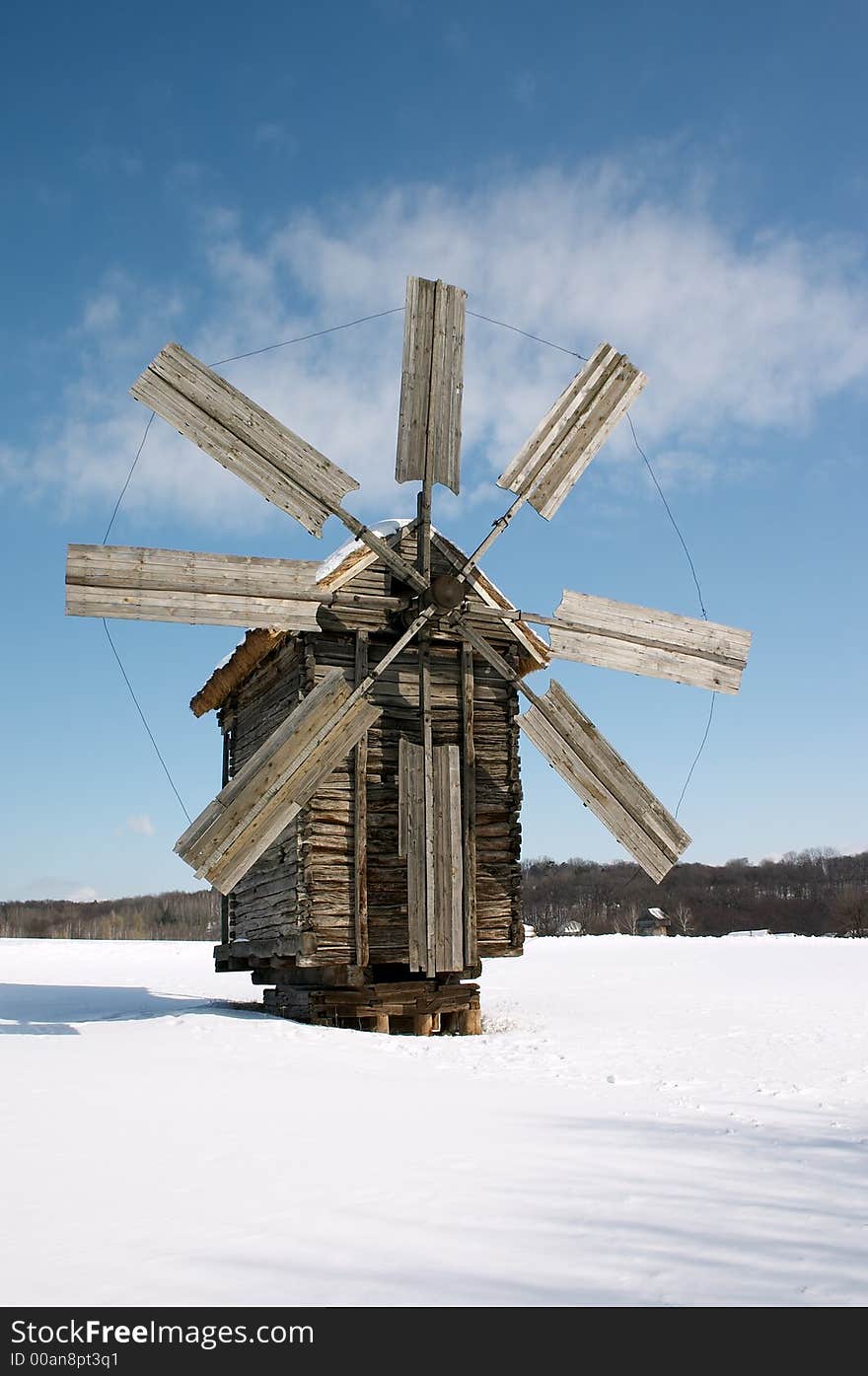 Wooden windmill on snow plain under blue sky