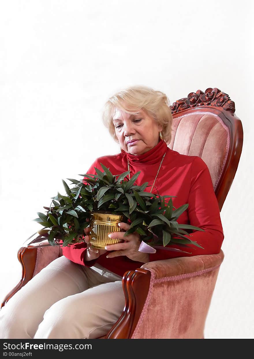 A senior citizen sitting in a armchair with a plant in her hand.