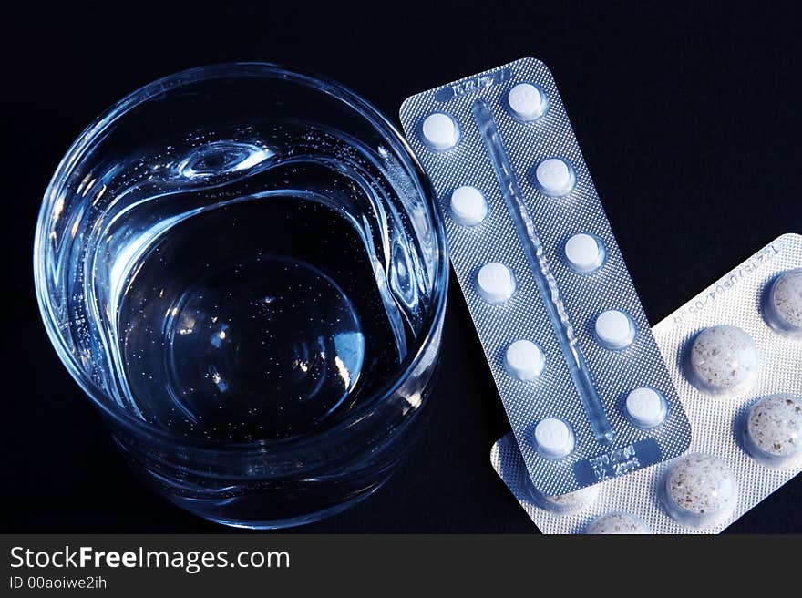 A glass of water and medicines on a dark background