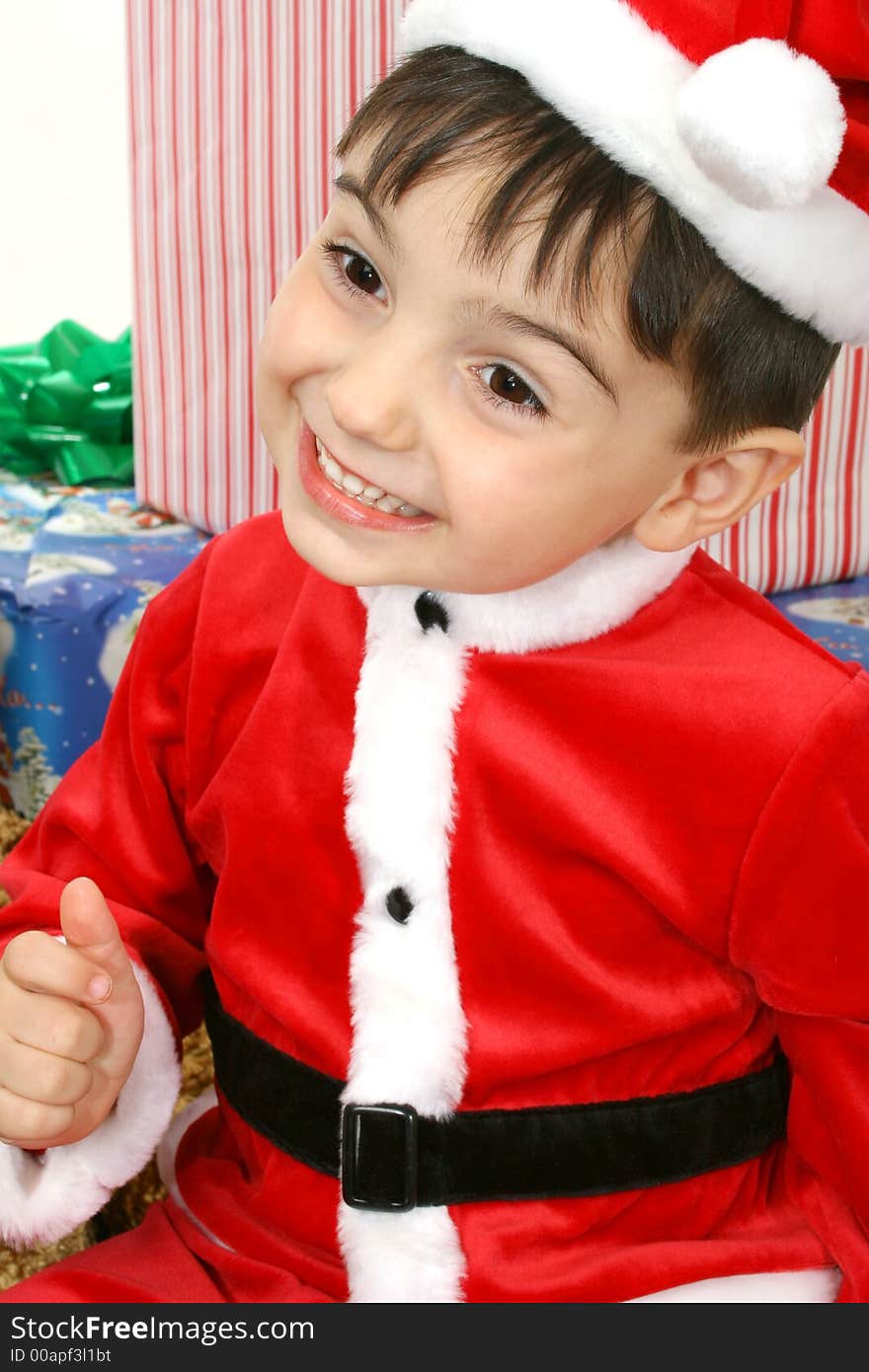 Toddler boy dressed in Santa suit sitting on packages.  Smiling. Toddler boy dressed in Santa suit sitting on packages.  Smiling.