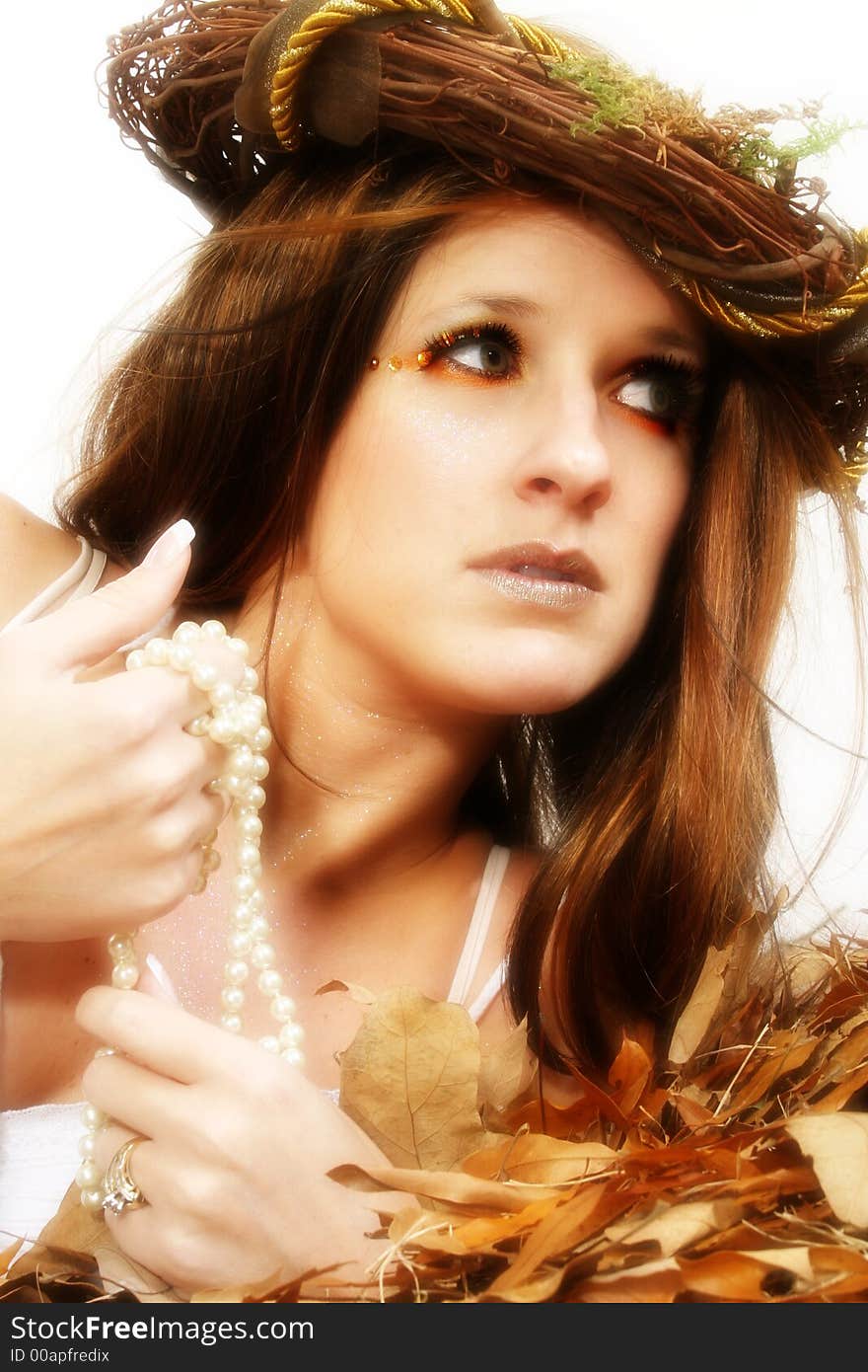 Beautiful young woman with leaves and glitter on face.  Sitting in leaves. Wearing white dress. Beautiful young woman with leaves and glitter on face.  Sitting in leaves. Wearing white dress.