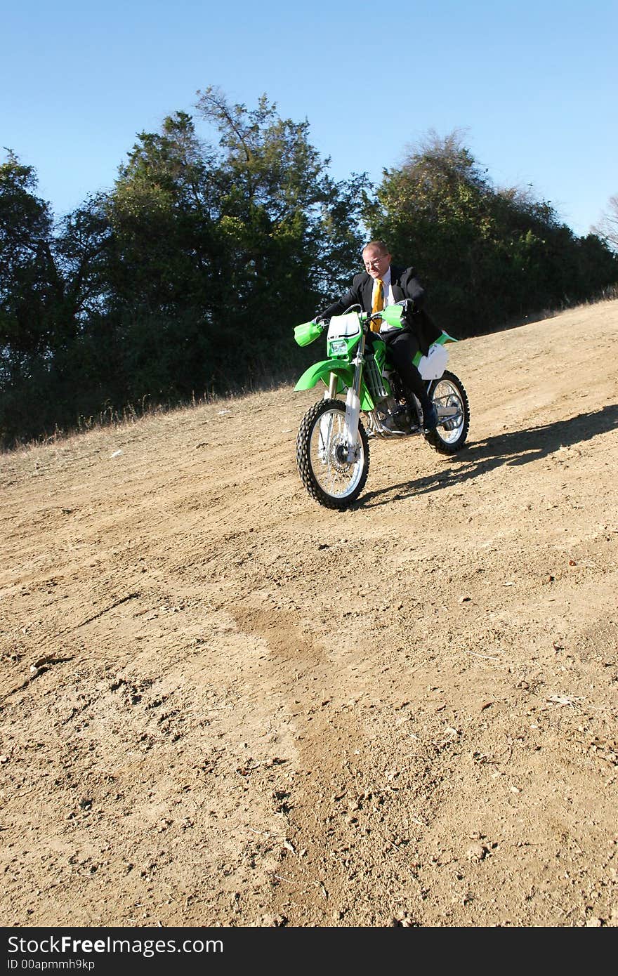 Thrity something business man in suit riding dirt bike on dirt riding track. Thrity something business man in suit riding dirt bike on dirt riding track.