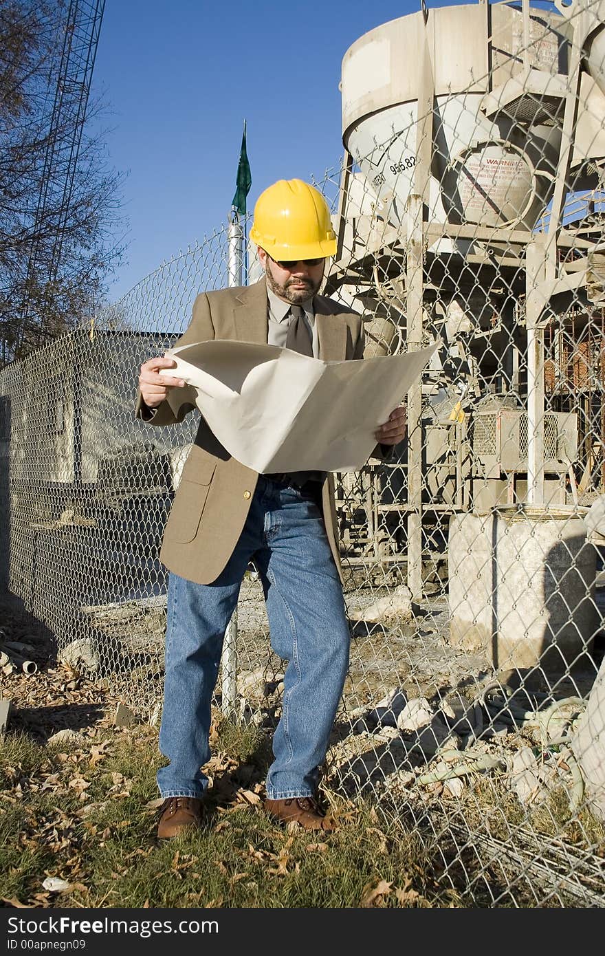 Man in suit at construction site holding bluerints and wearing yellow hardhat. Man in suit at construction site holding bluerints and wearing yellow hardhat.