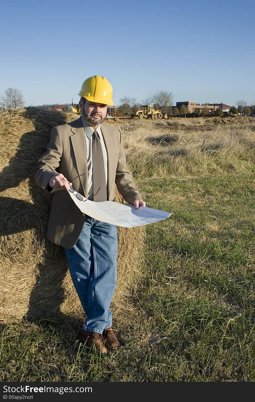 Man in suit at construction site holding bluerints and wearing yellow hardhat. Man in suit at construction site holding bluerints and wearing yellow hardhat.