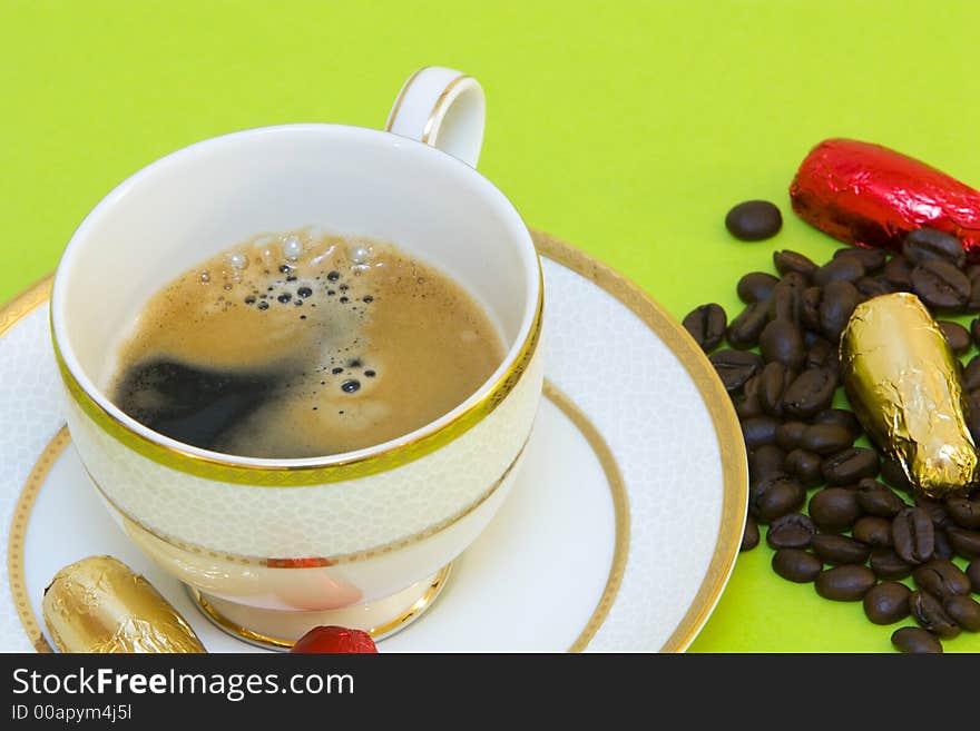 Coffee cup on green background, chocolates and coffeebeans. Coffee cup on green background, chocolates and coffeebeans