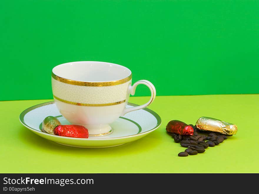 Coffee cup on green background, chocolates and coffeebeans. Coffee cup on green background, chocolates and coffeebeans