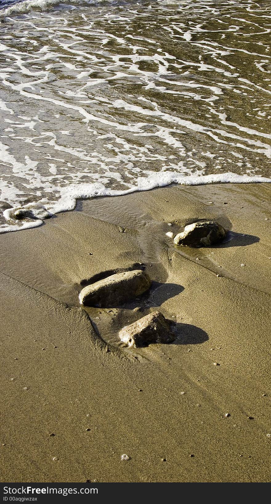 Brown sandy beach with three stones washed ove by retreating sea water. Brown sandy beach with three stones washed ove by retreating sea water