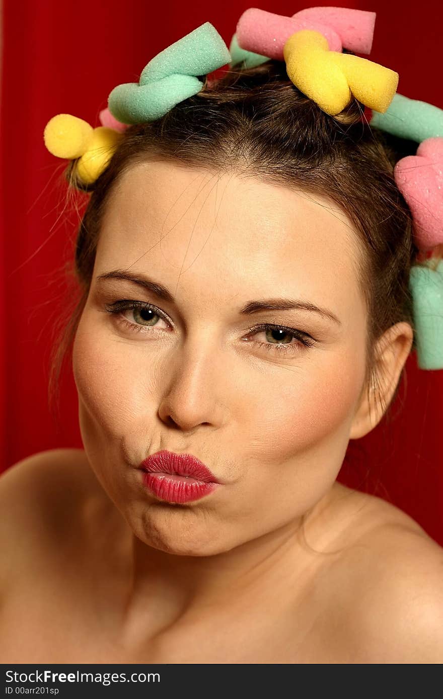 Close up of young woman with colourful curlers in her hair and red lips