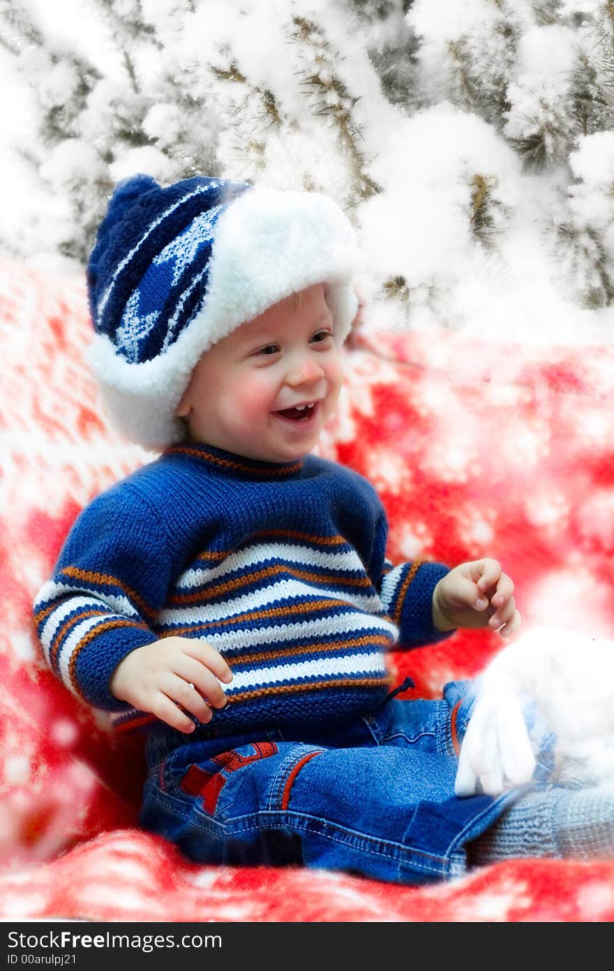 Happy smiling young boy sitting on the red cover under the snowy evergreen. Happy smiling young boy sitting on the red cover under the snowy evergreen