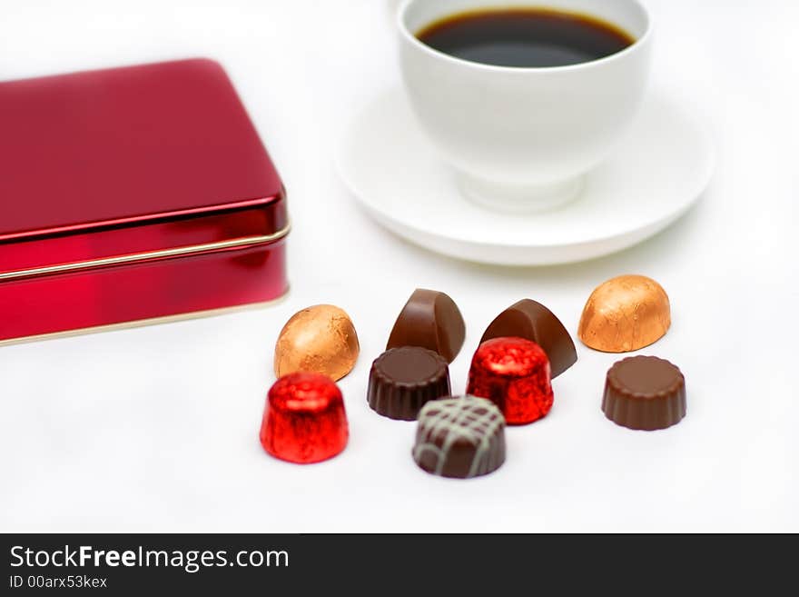 Elegant chocolates, a red box and a cup of coffee over white background-festive still life.Selective focus on some chocolates pieces. Elegant chocolates, a red box and a cup of coffee over white background-festive still life.Selective focus on some chocolates pieces.