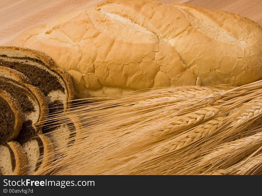 Close up of two different kinds of bread and some wheat on a wood cutting board. Close up of two different kinds of bread and some wheat on a wood cutting board