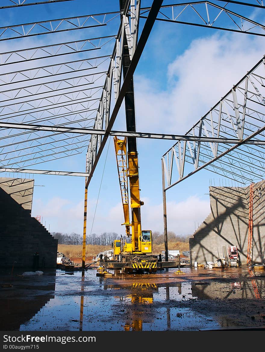 A yelow crane on a construction site with a blue sky background. A yelow crane on a construction site with a blue sky background