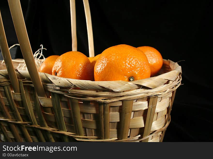 Clementines imported from Spain in a basket on a black background.  These are also knows as Satsumas and are grown in southern Louisiana.