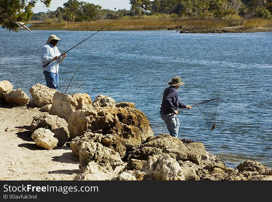 Two men catch fish with poles and nets on the riverbank. Two men catch fish with poles and nets on the riverbank.