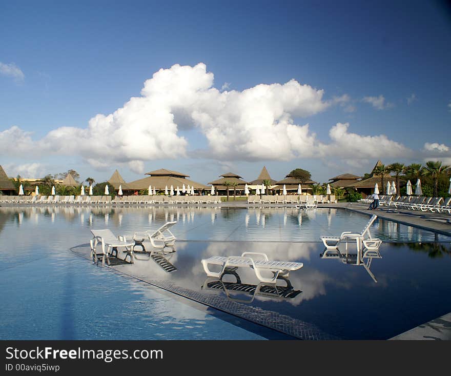 Stunning luxury pool at holiday resort with loungers and clouds reflected in the water. Stunning luxury pool at holiday resort with loungers and clouds reflected in the water