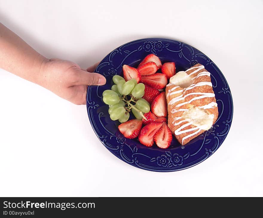 Pastry, grapes and strawberry on a blue plate holding by hand